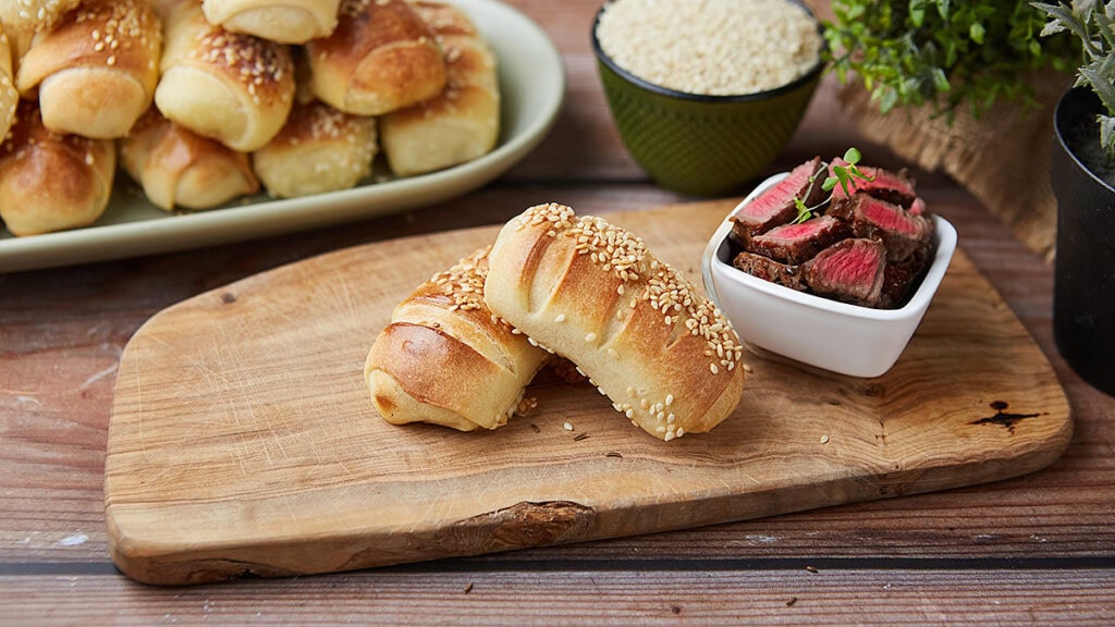 Domaće kiflice sa sezamom i punjenjem na drvenoj dasci.